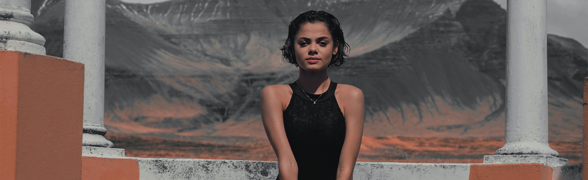 Frau mit kurzen, dunklen Haaren blickt vor einer Bergkulisse in die Kamera.